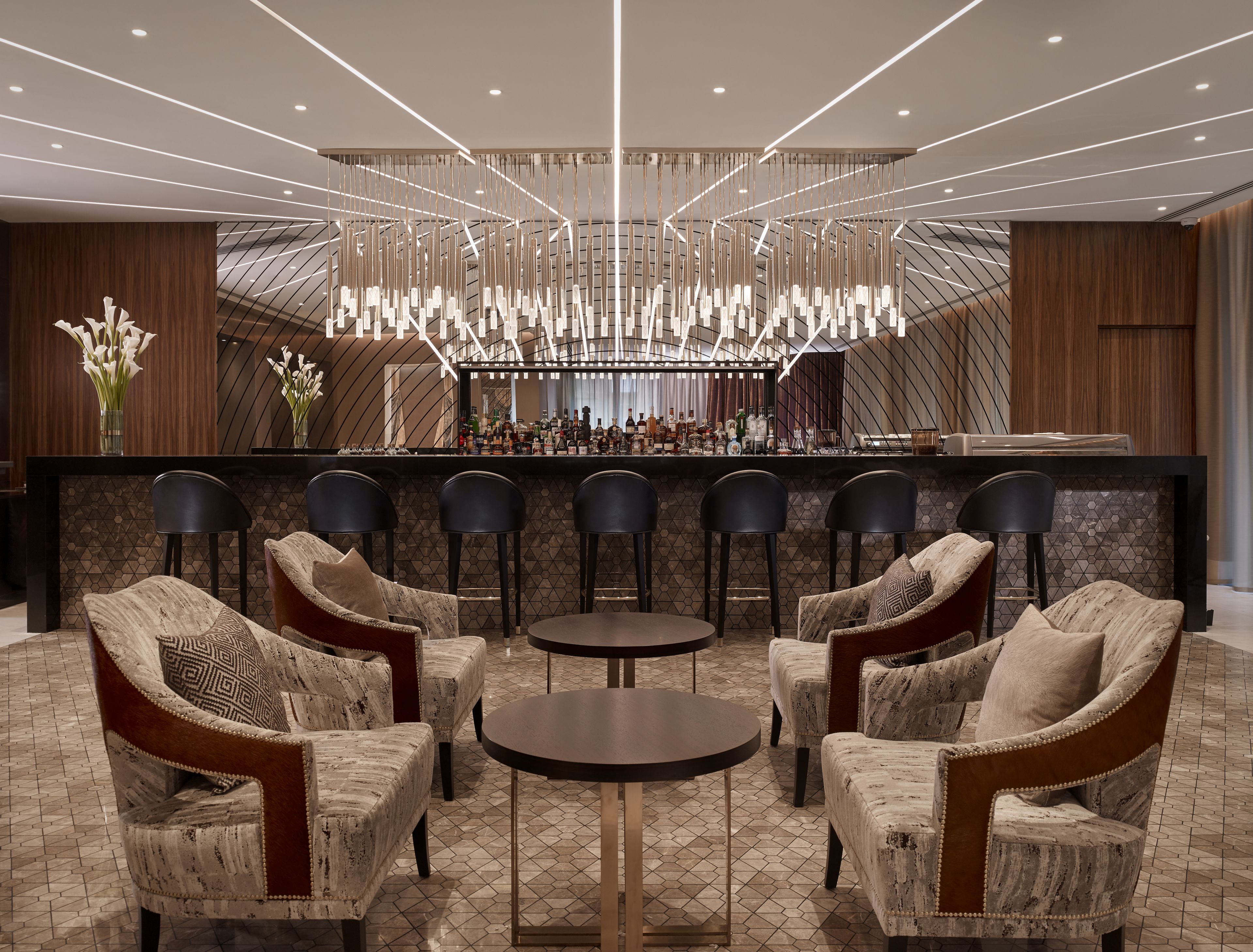 A modern bar area with a high ceiling, geometric light fixtures, and a bar counter with stools.