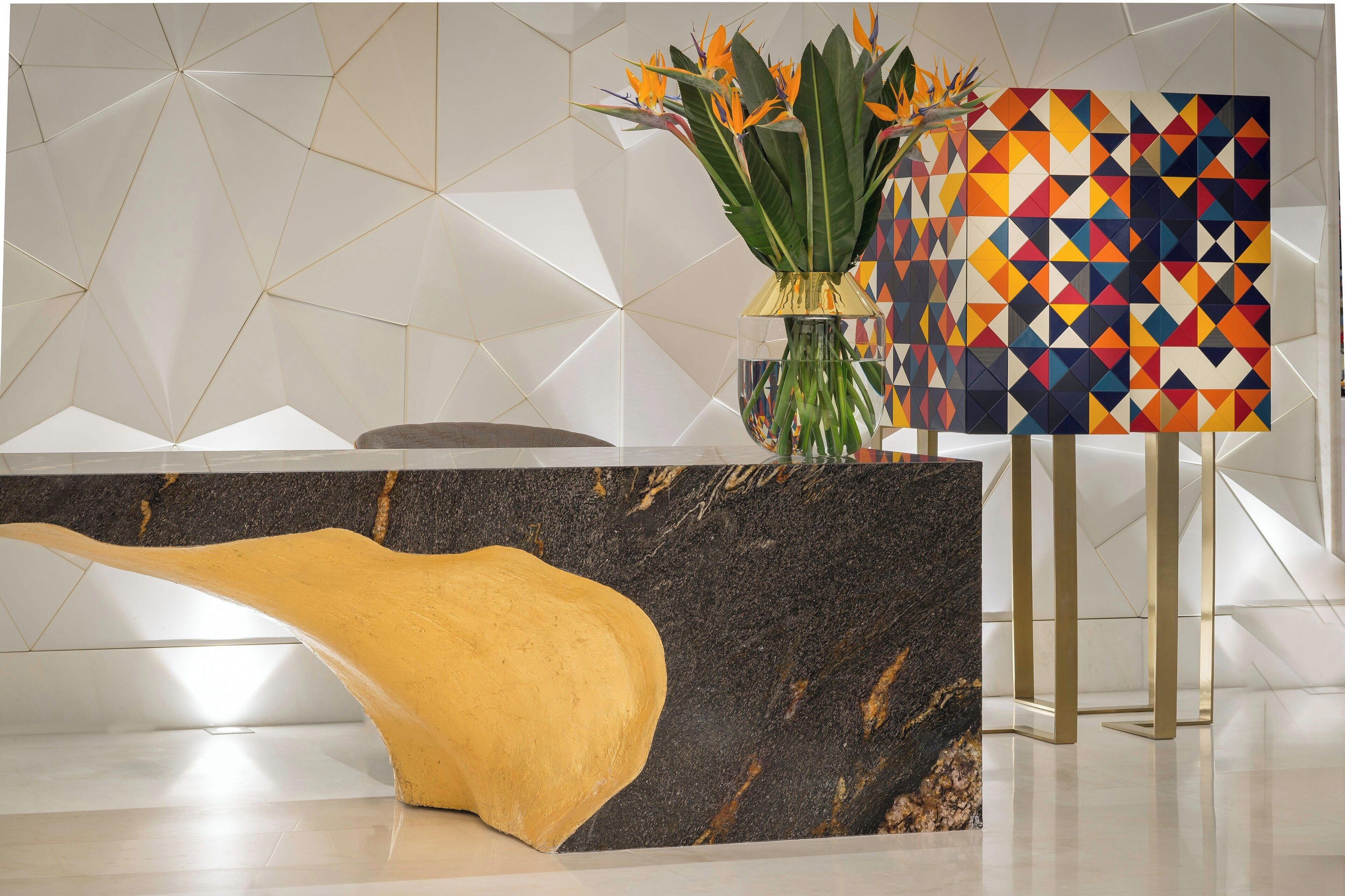Un área de recepción con un mostrador de mármol, un florero con flores y una pared con diseño geométrico.