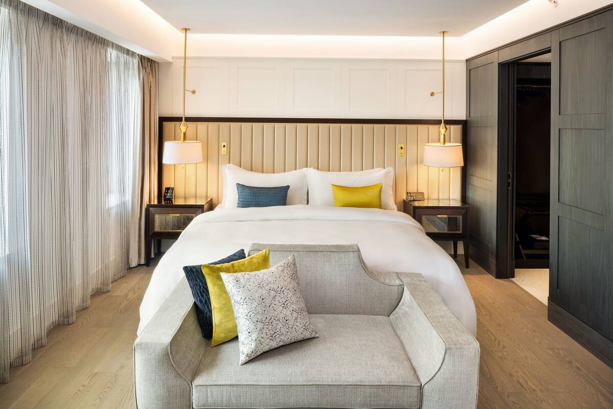 A modern hotel room with a large bed, two bedside tables, a chair, and a wardrobe.