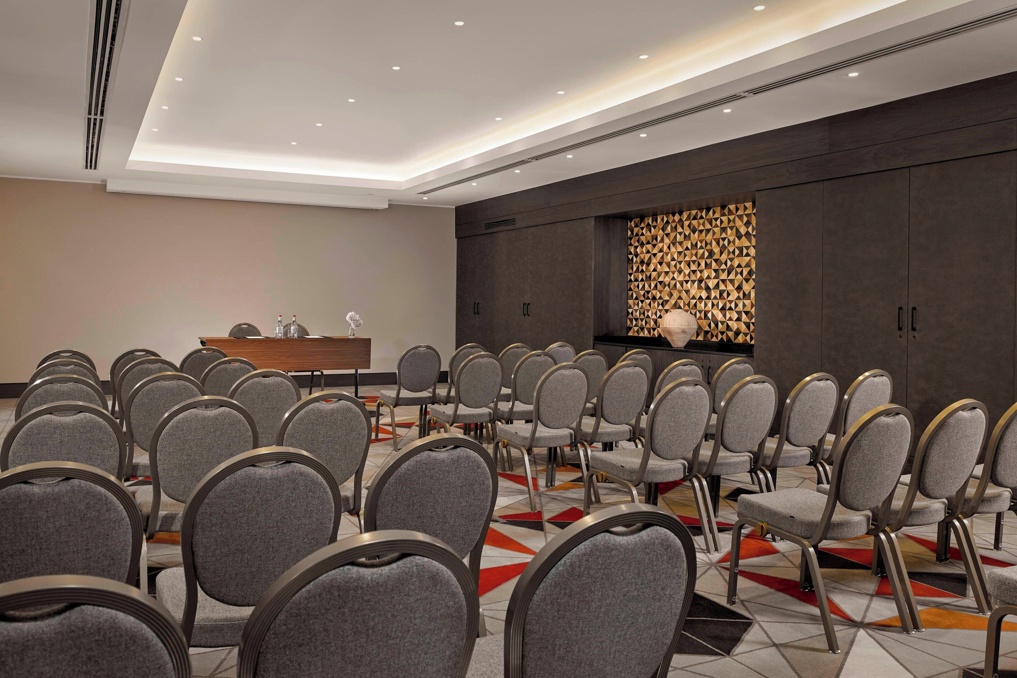 Ein Konferenzraum mit grauen Stühlen, einem Holztisch und einer Wand mit Muster.