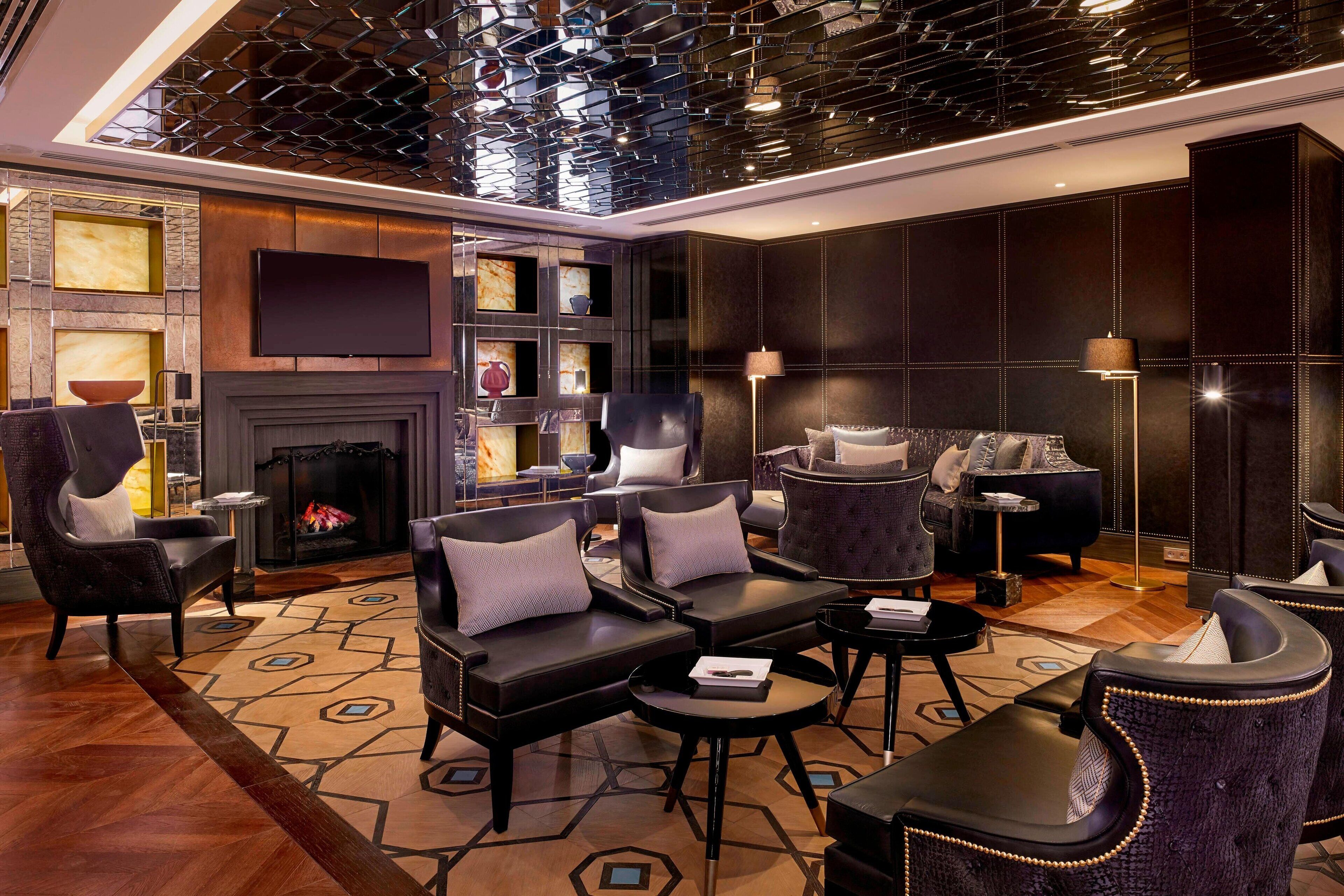 A modern living room with a fireplace, leather sofas, a flat-screen TV, and a patterned rug.