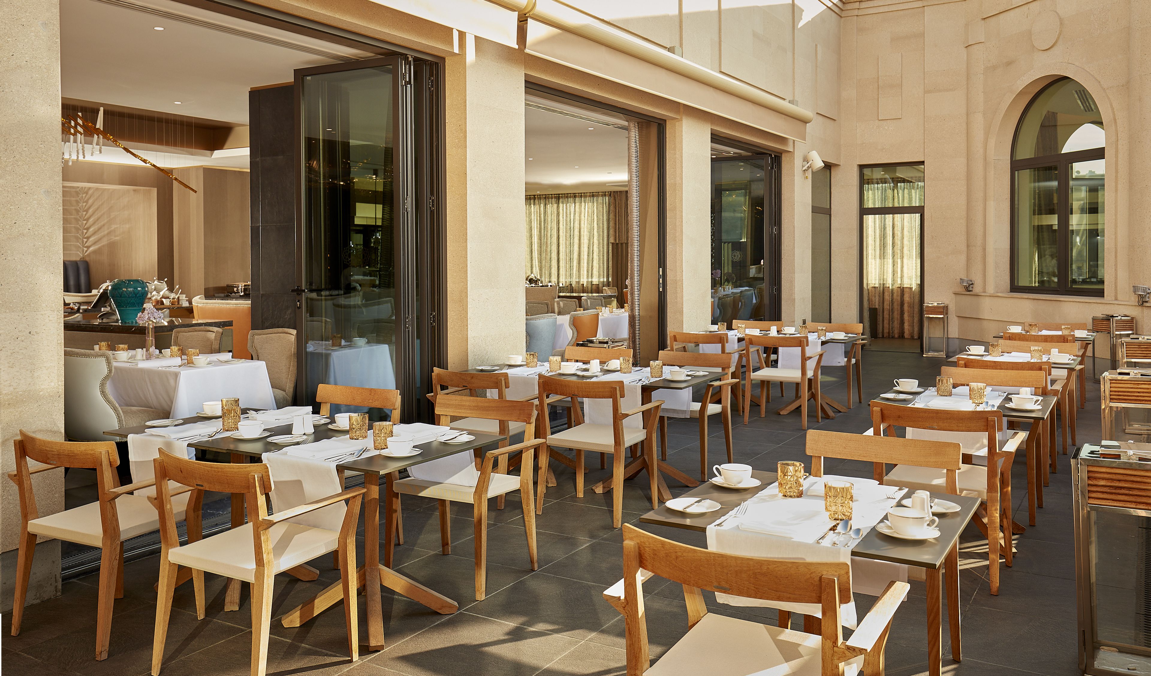 Un restaurante con terraza, mesas cubiertas con manteles blancos y sillas de madera.