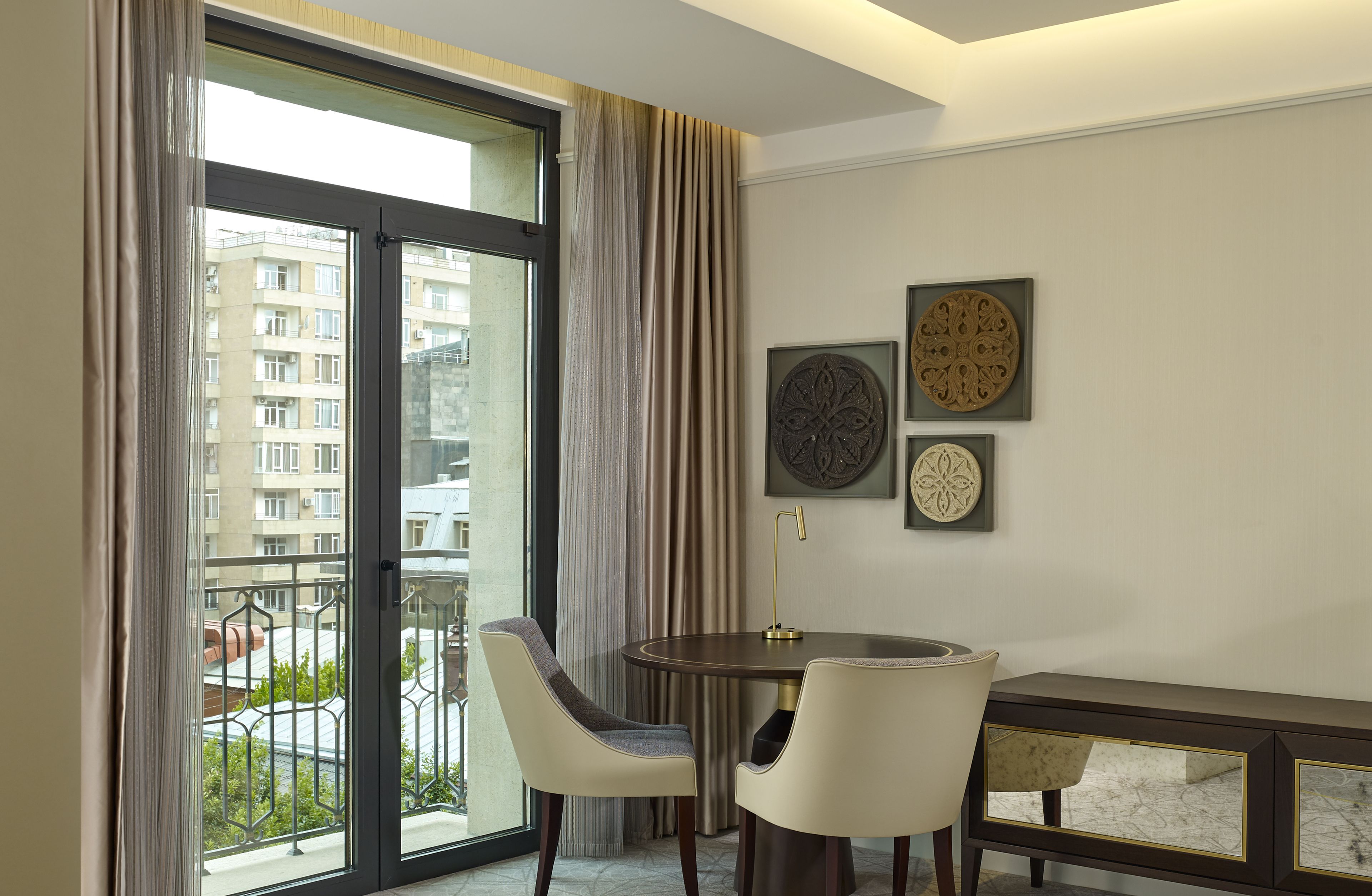 A modern room with a large sliding glass door, two chairs, a round table, and decorative wall art.