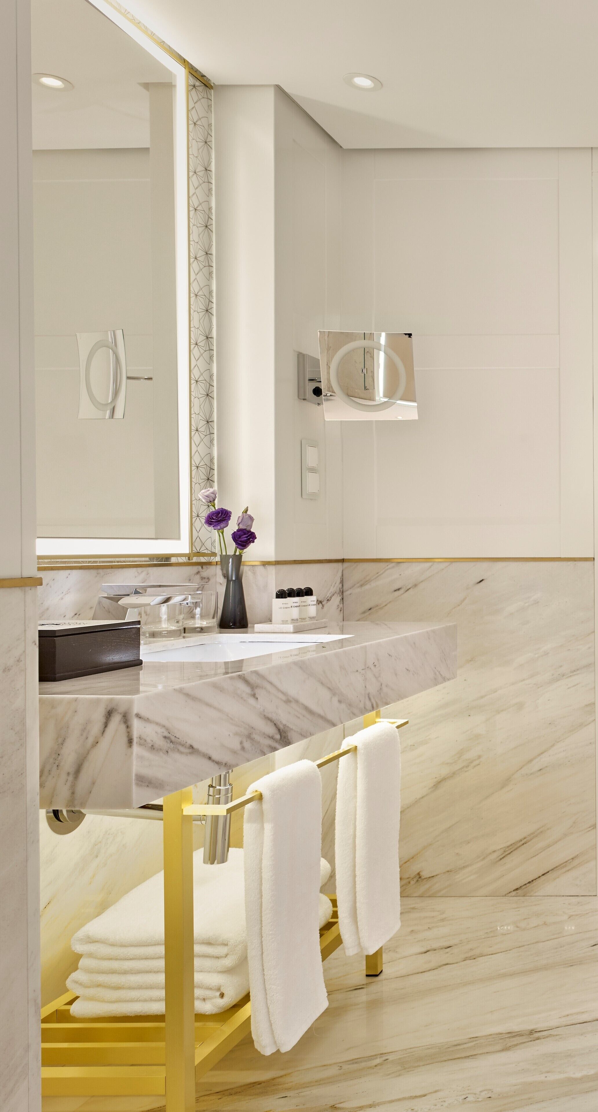 A modern bathroom with a marble vanity, a large mirror, and a towel rack.