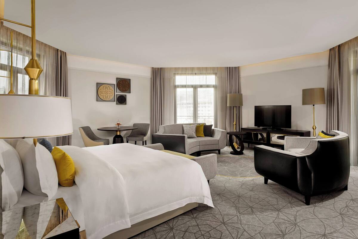 A hotel room with a bed, a sofa, a desk, a TV, and a lamp.