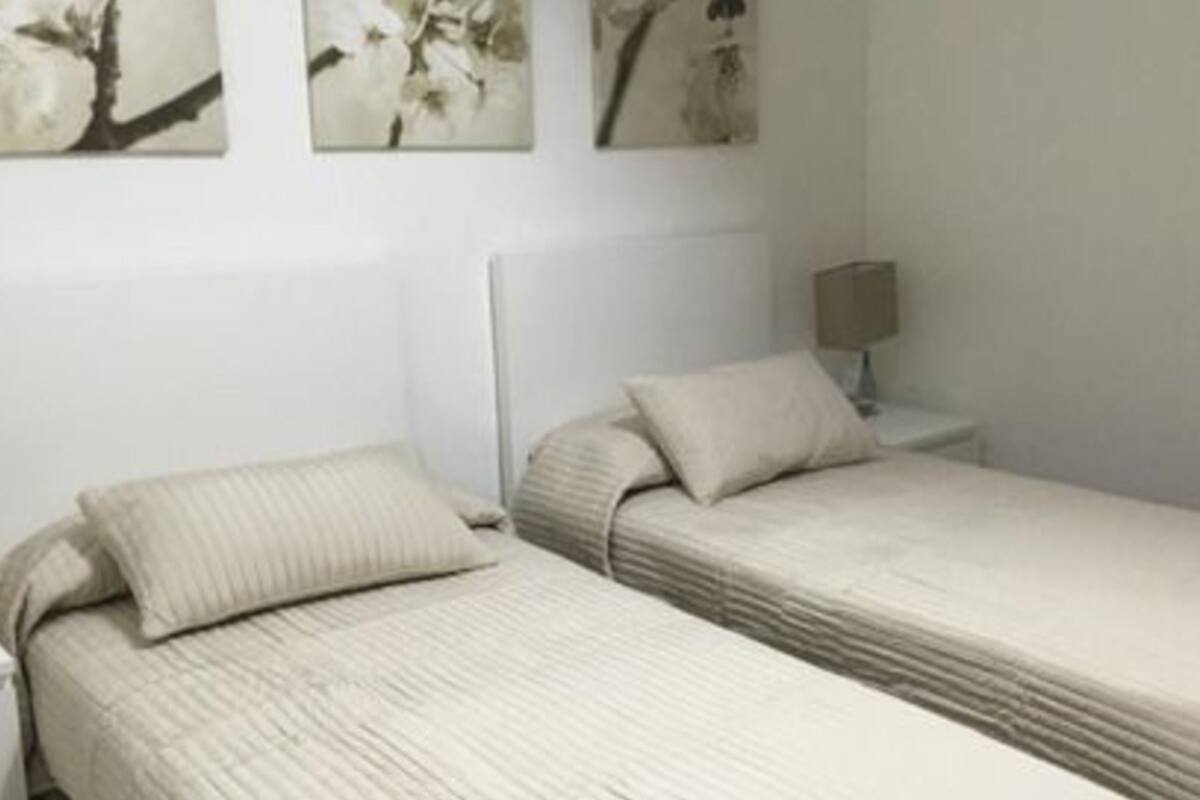 A single-bed room with a headboard, a bedside table, and a lamp. There are three wall-mounted artworks above the bed.