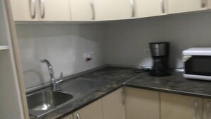Una cocina con armarios color beige, un lavamanos de acero inoxidable, una cafetera y un microondas.