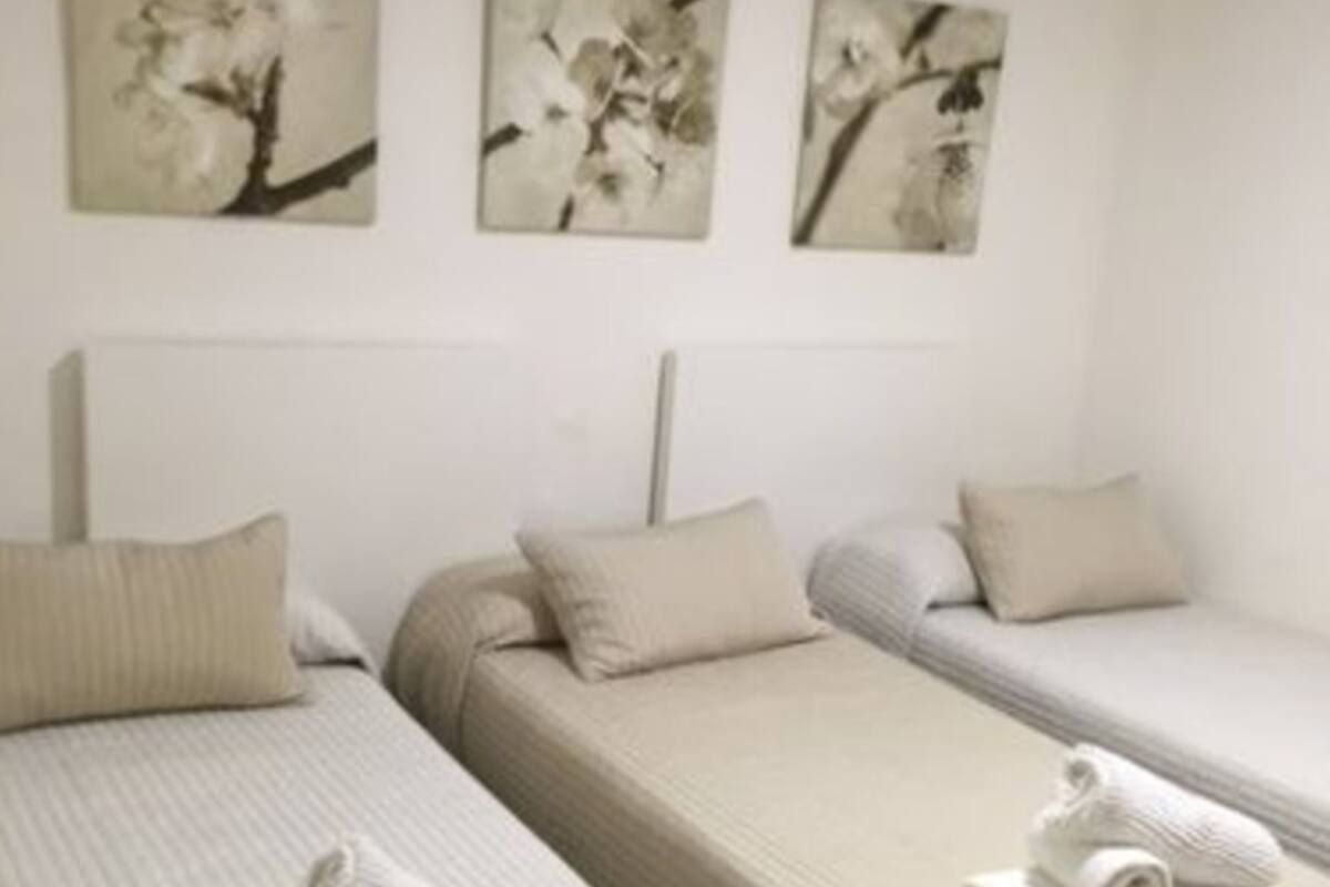 A hotel room with two single beds, each with a pillow and a rolled towel. There are three wall-mounted paintings above the beds.