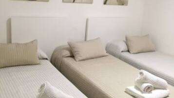 Habitación de hotel con dos camas individuales, cada una con una almohada y una toalla enrollada. Hay tres cuadros colgados en la pared sobre las camas.