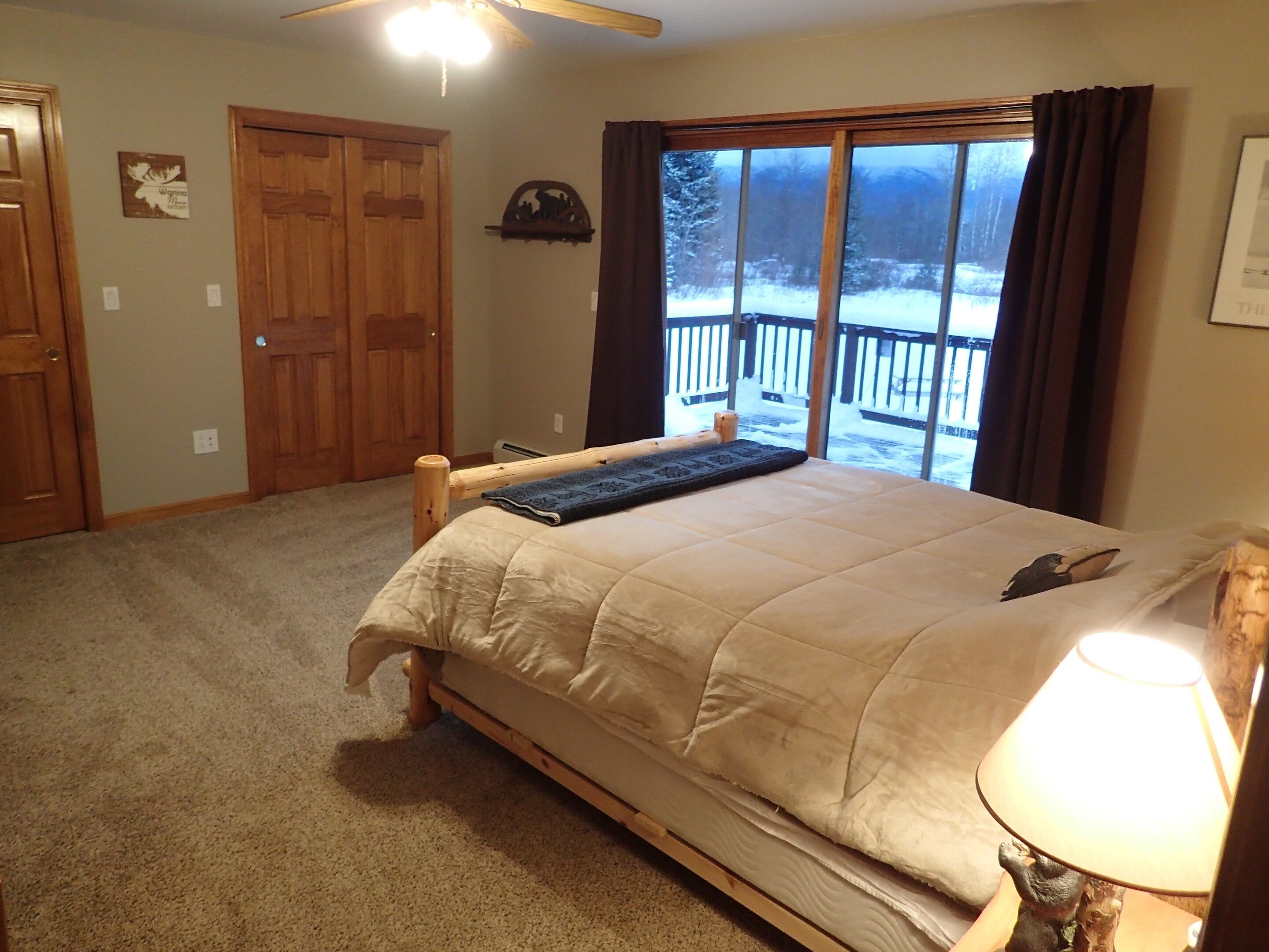 Ein Schlafzimmer mit Bett, einem Fenster mit Blick auf ein verschneites Deck, einer Holztür und einem an der Wand befestigten Regal.