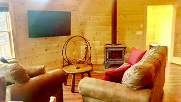A cozy cabin interior with a wooden interior, a fireplace, a sofa, and a television.