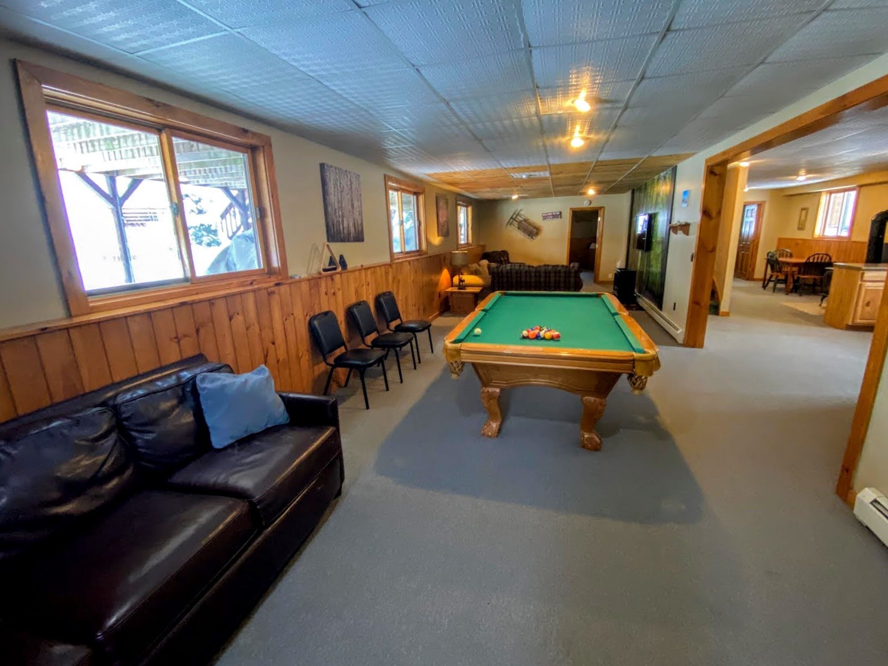 Une table de billard dans une pièce où se trouvent un banc en bois, un canapé et, au fond, un coin repas.