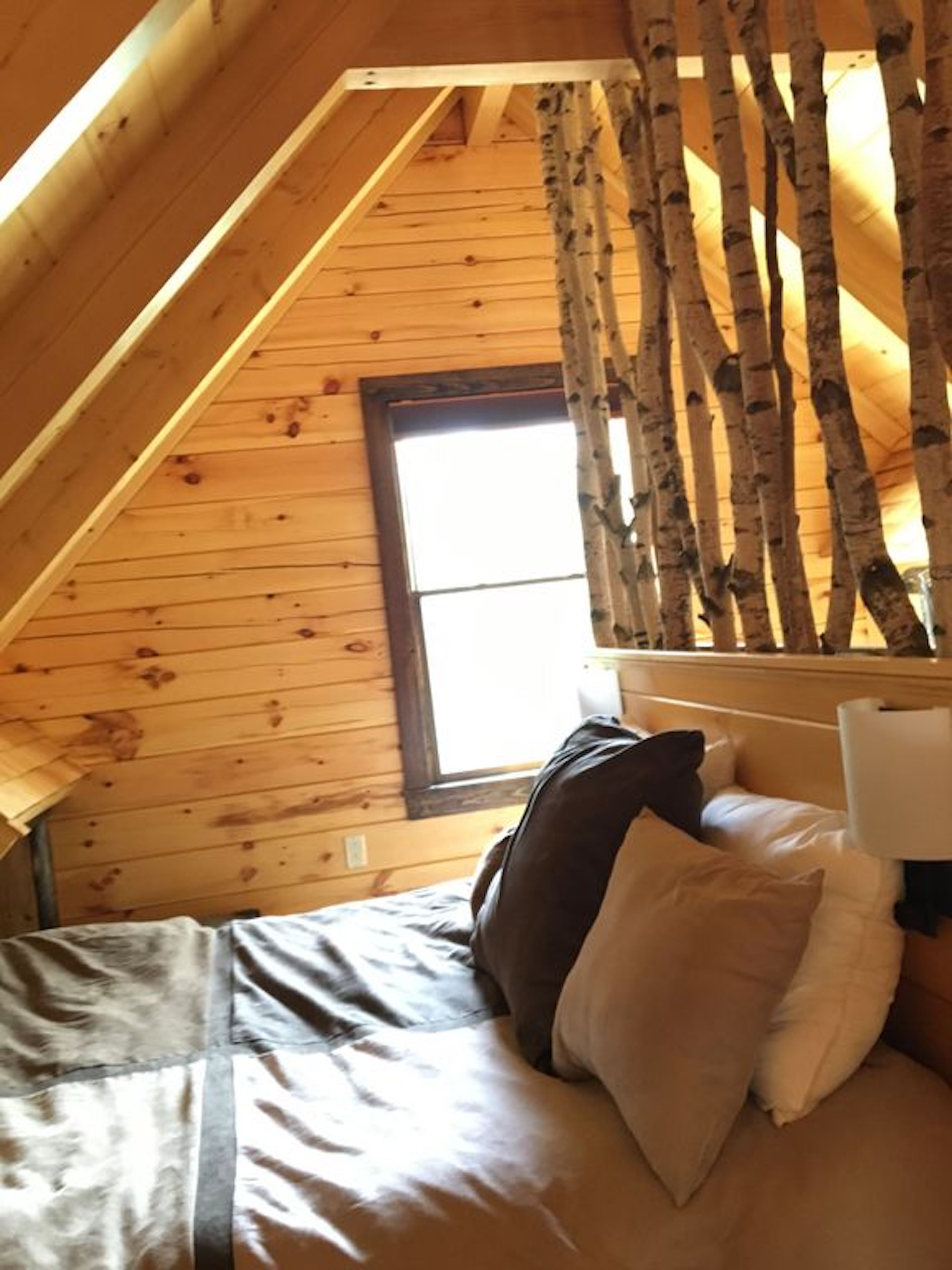 Un dormitorio acogedor con techo inclinado, paredes de madera, una ventana y una cama con almohadas.