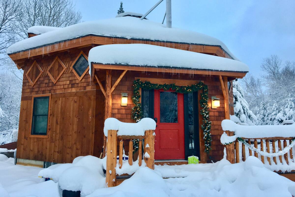 Une cabane en bois avec une porte rouge, entourée de neige.