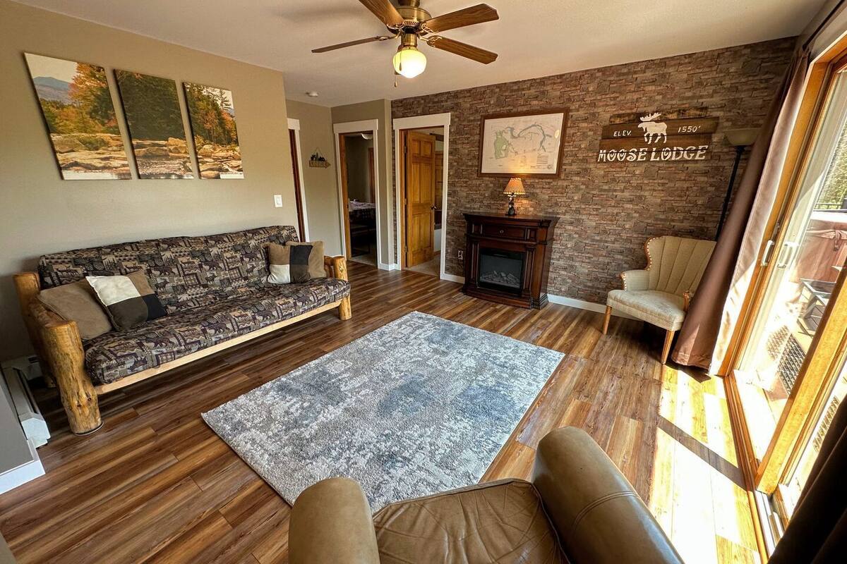 Un salon chaleureux avec un plancher en bois, un canapé à motifs, une cheminée et une grande fenêtre.