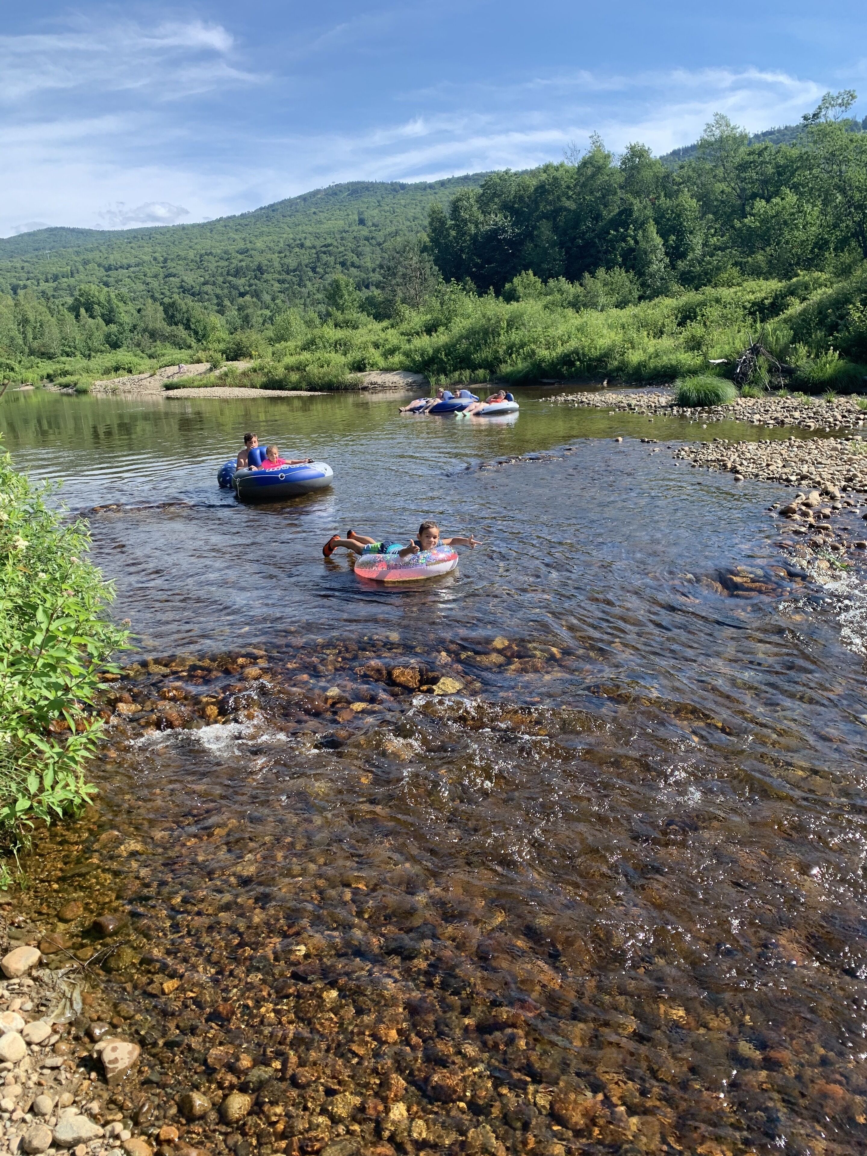 Une rivière aux eaux claires, bordée de verdure et entourée de collines.