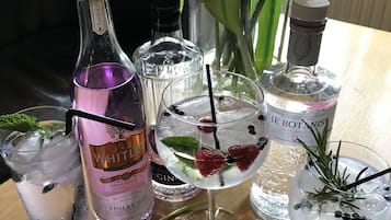 Una mesa con varias botellas de ginebra, dos vasos con hielo y bayas, y un florero con flores.