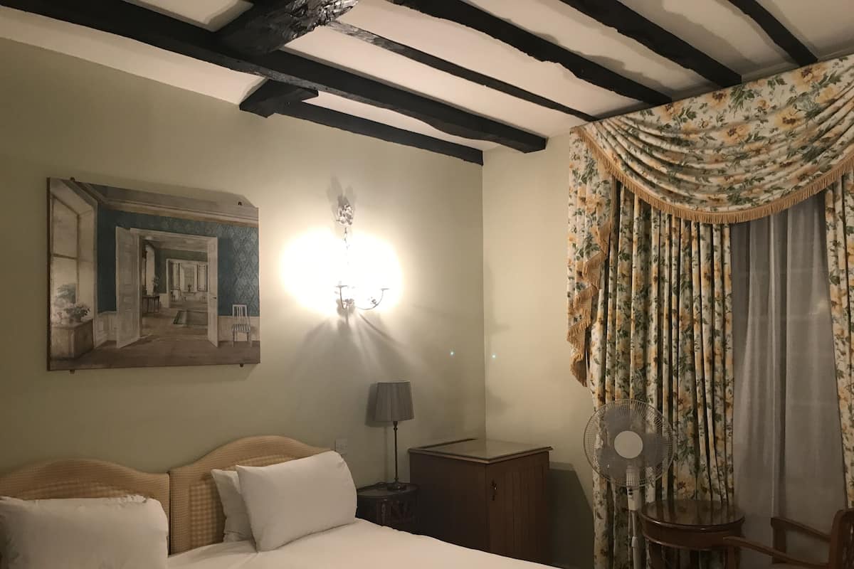 Quarto de hotel com cama, mesa de cabeceira, abajur, ventilador e espelho.