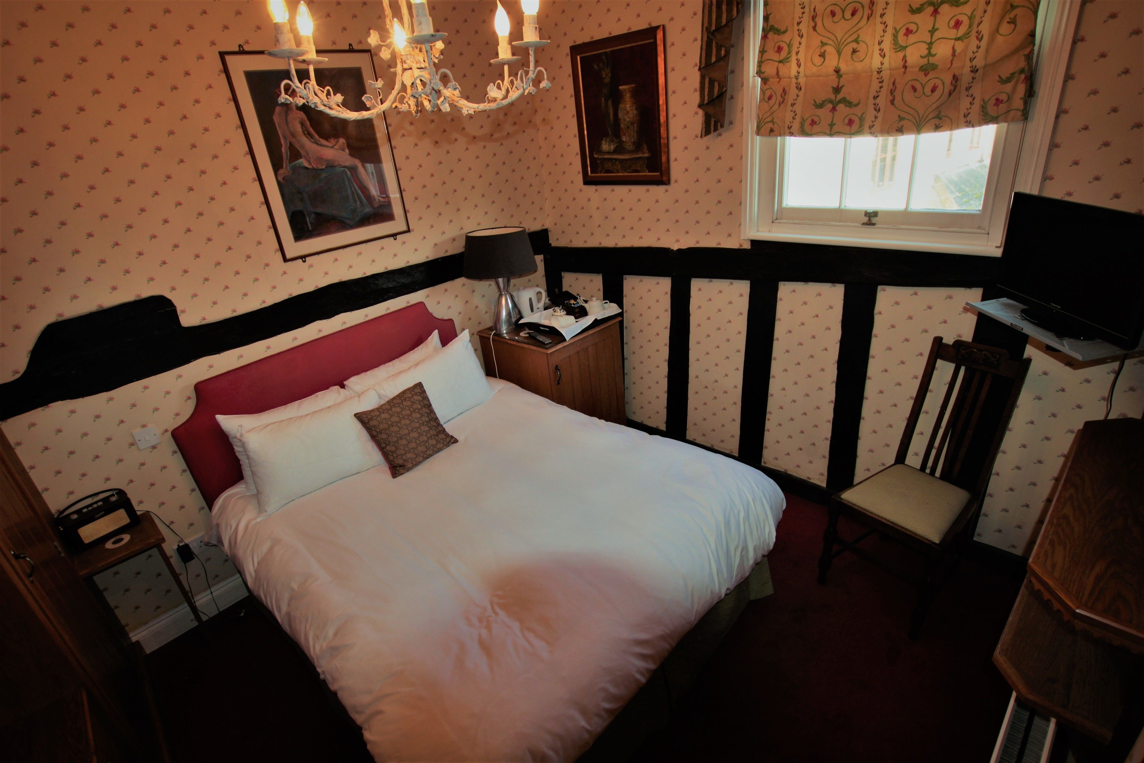 A bedroom with a large bed, a nightstand, a chair, a desk, and a window with curtains.