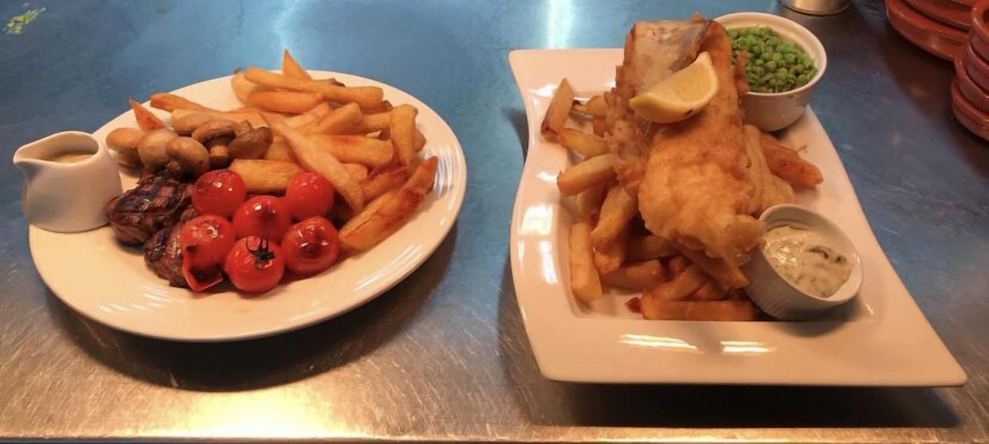 Dos platos de comida, uno con papas fritas y tomates y otro con pescado y guisantes.