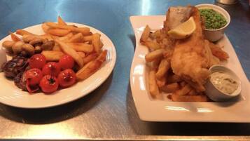Dos platos de comida, uno con papas fritas y tomates y otro con pescado y guisantes.