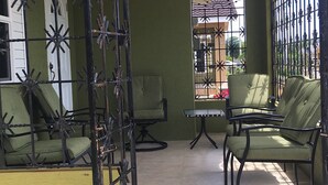 Ein Patio mit zwei grünen, gepolsterten Stühlen und einem kleinen Tisch, umgeben von einem Metallzaun mit Verzierungen.