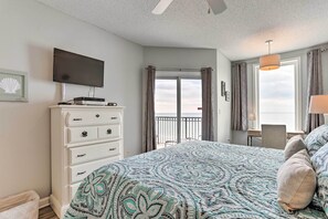 Ein Schlafzimmer mit Bett, Kommode, Fernseher, Schreibtisch mit Stuhl und einem Balkon mit Vorhängen.