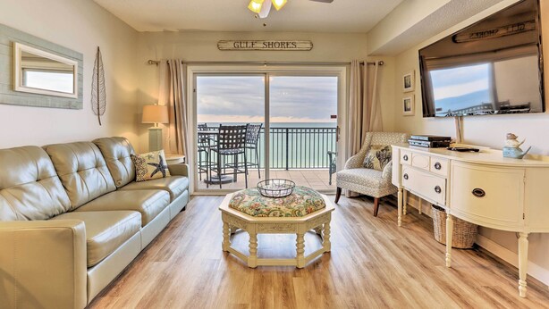 A living room with a leather sofa, a round table with a floral tablecloth, a white cabinet, and a ceiling fan. - Beachfront Gulf Shores Condo w/ Pool (Gulf Shores)