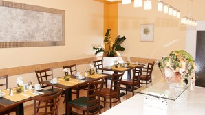 A restaurant with multiple tables and chairs, a large potted plant, and a framed picture on the wall. - Hotel Wendelstein (Wendelstein)