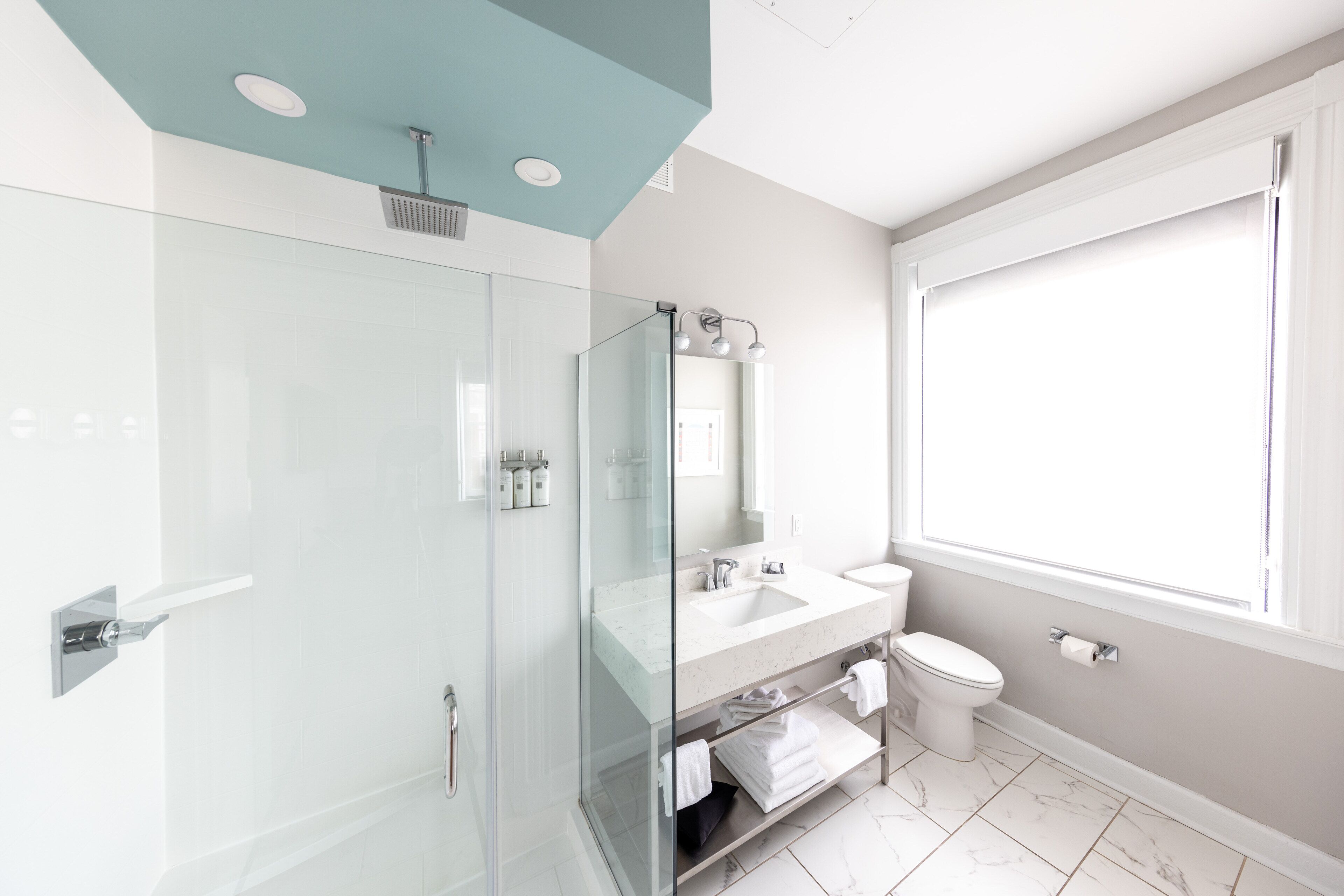 Un baño moderno con cabina de ducha de vidrio, tocador con lavamanos y espejo, y un inodoro.