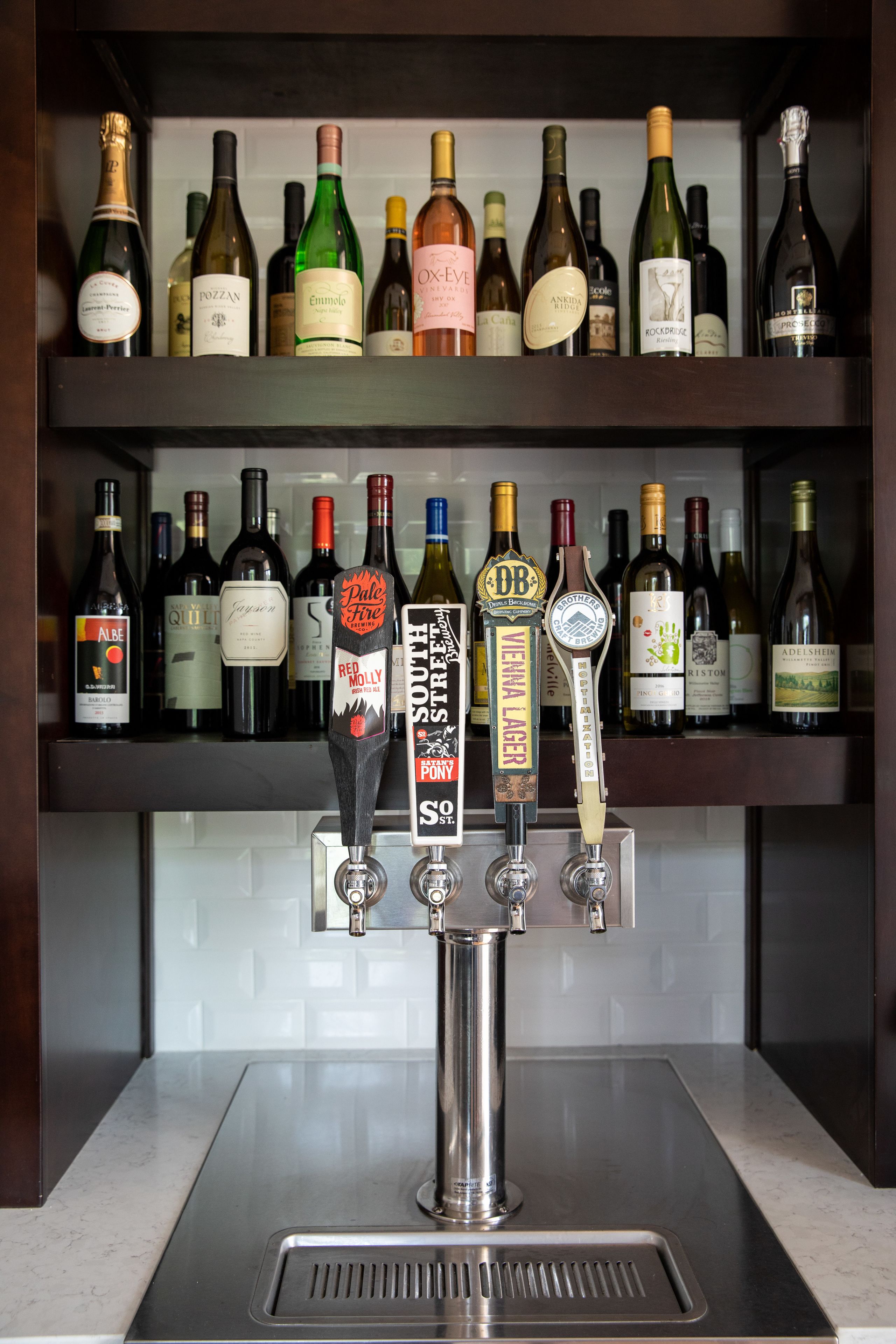 A bar area with multiple shelves of wine bottles and a tap with various beer options.