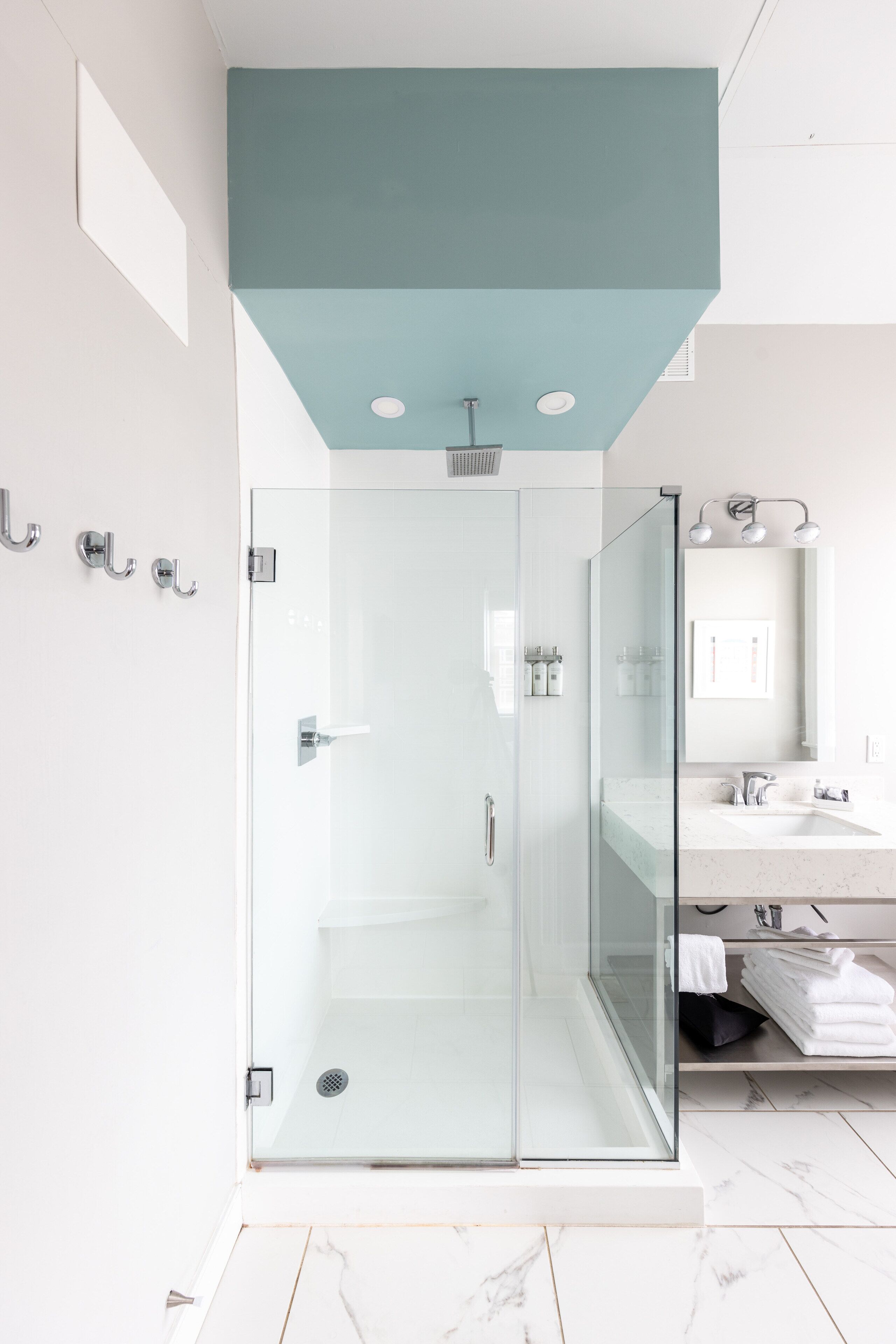 A modern bathroom with a glass-enclosed shower, a white sink, and a teal accent wall.