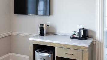 A small kitchenette with a coffee maker, a mini fridge, and a flat-screen TV mounted on the wall.