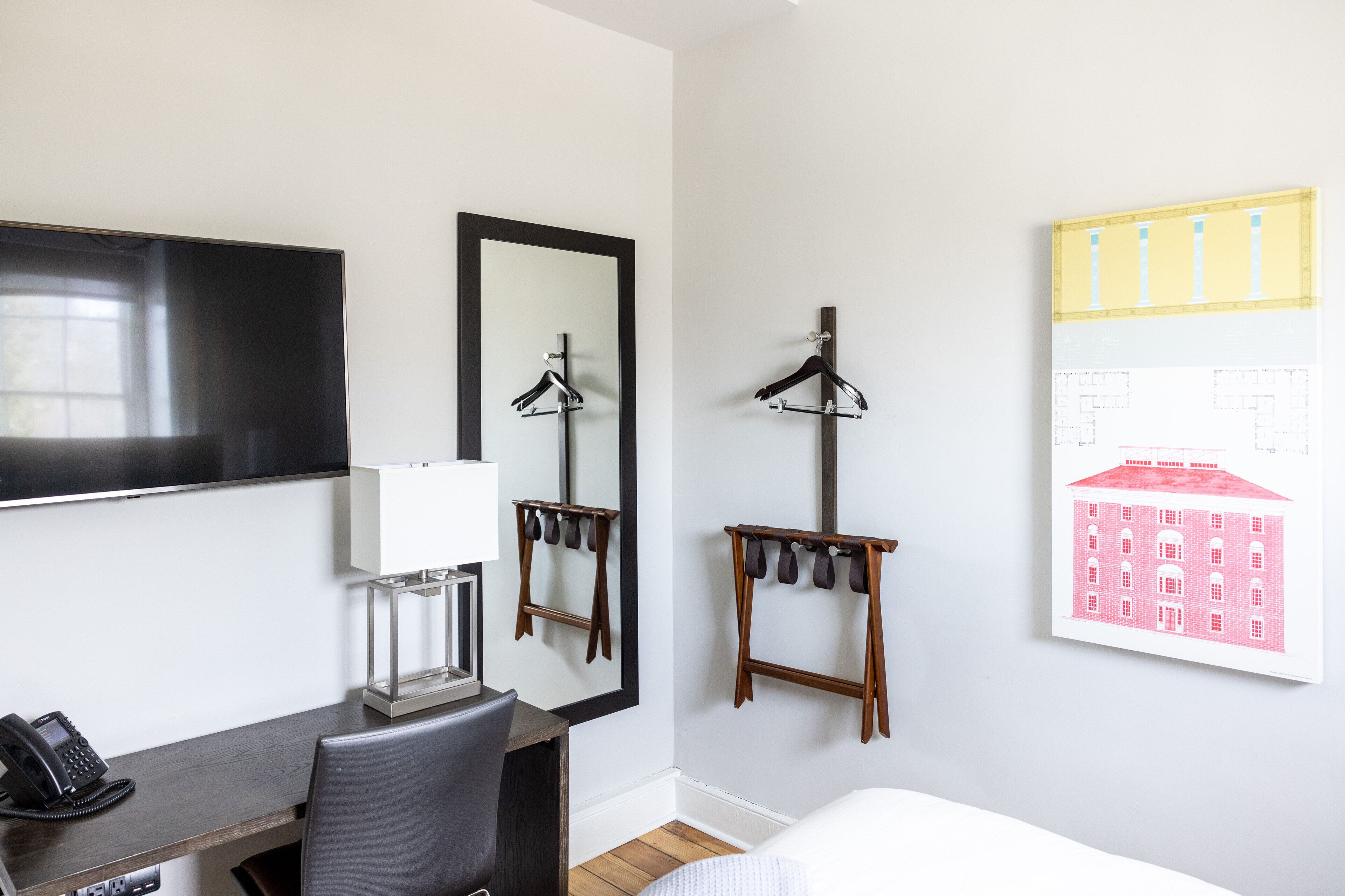 Una habitación de hotel con escritorio, silla, teléfono, espejo y una obra de arte en la pared.