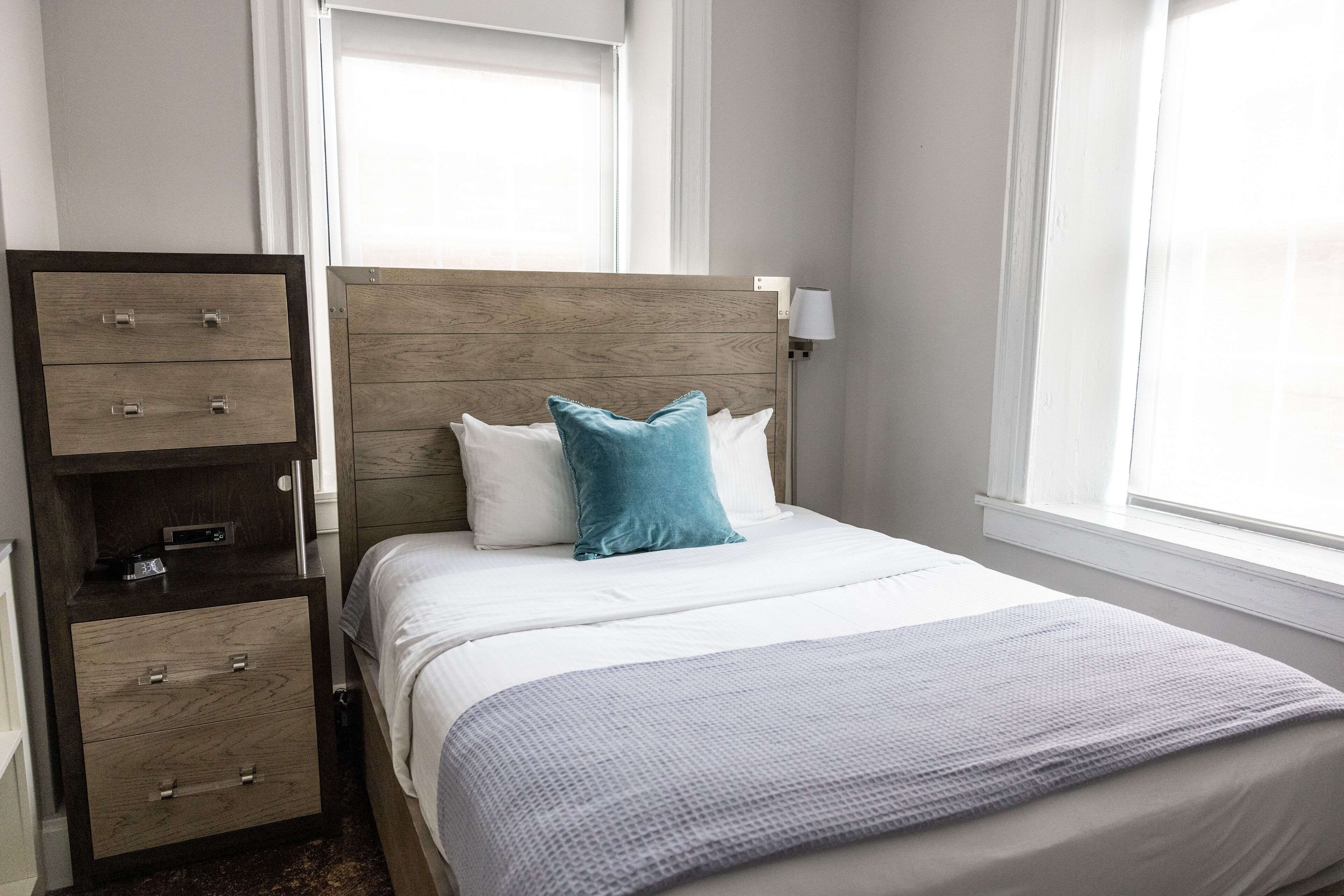 Een keurig opgemaakt bed met een houten hoofdbord, een nachtkastje met lades en een bedlampje.