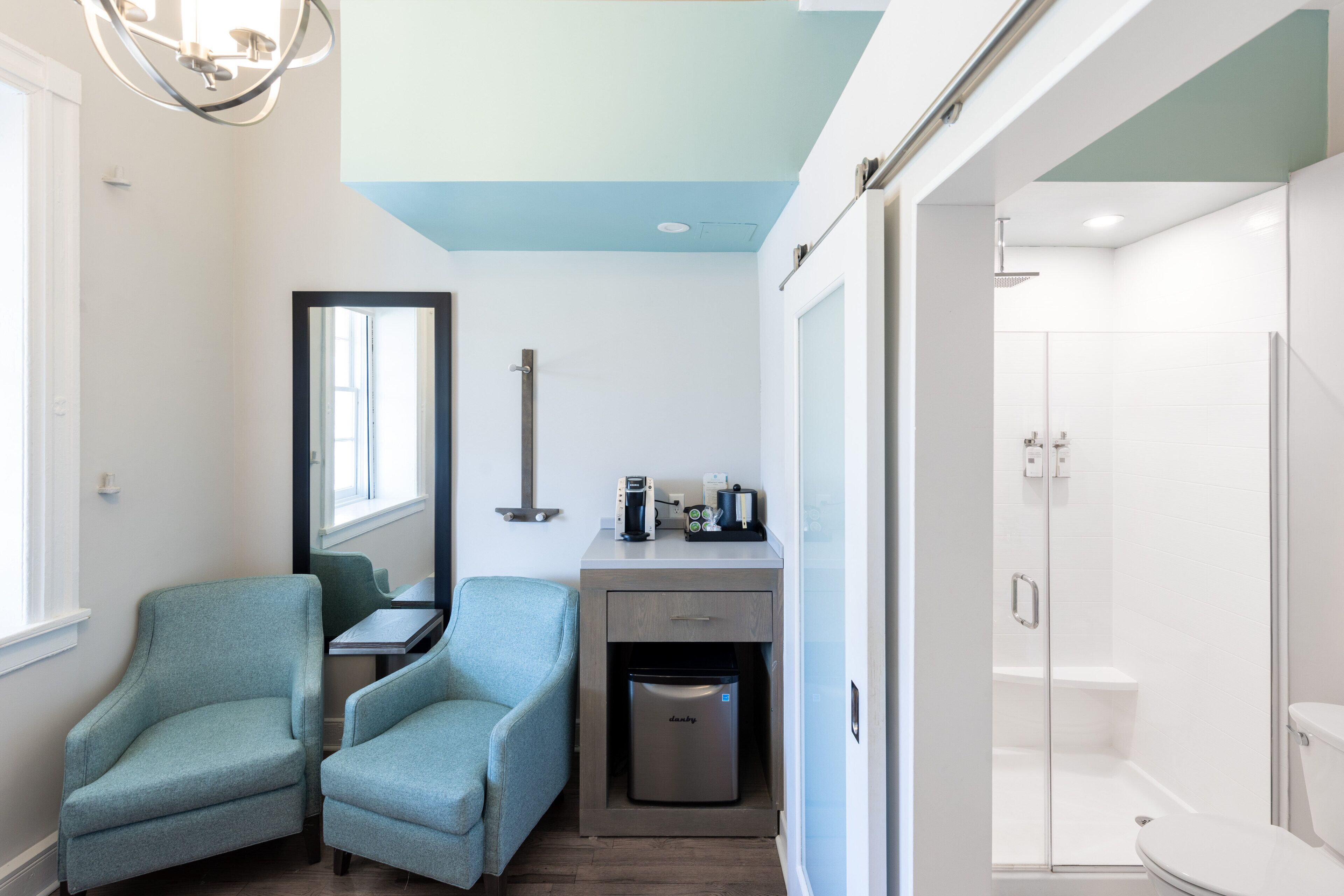 A bathroom with a shower, toilet, and a small seating area with chairs and a coffee machine.
