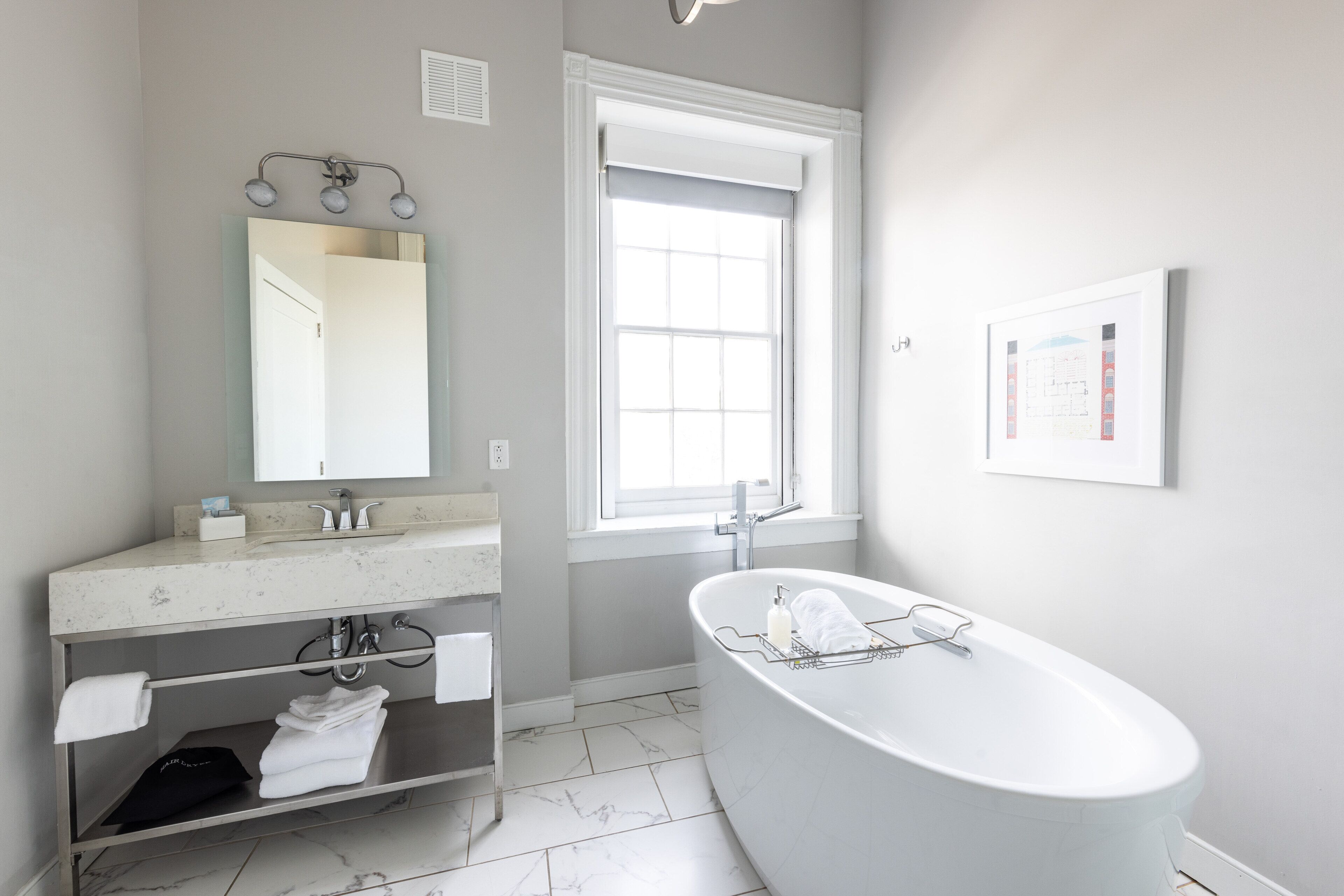 A modern bathroom with a freestanding bathtub, a vanity with a mirror, and a window providing natural light.