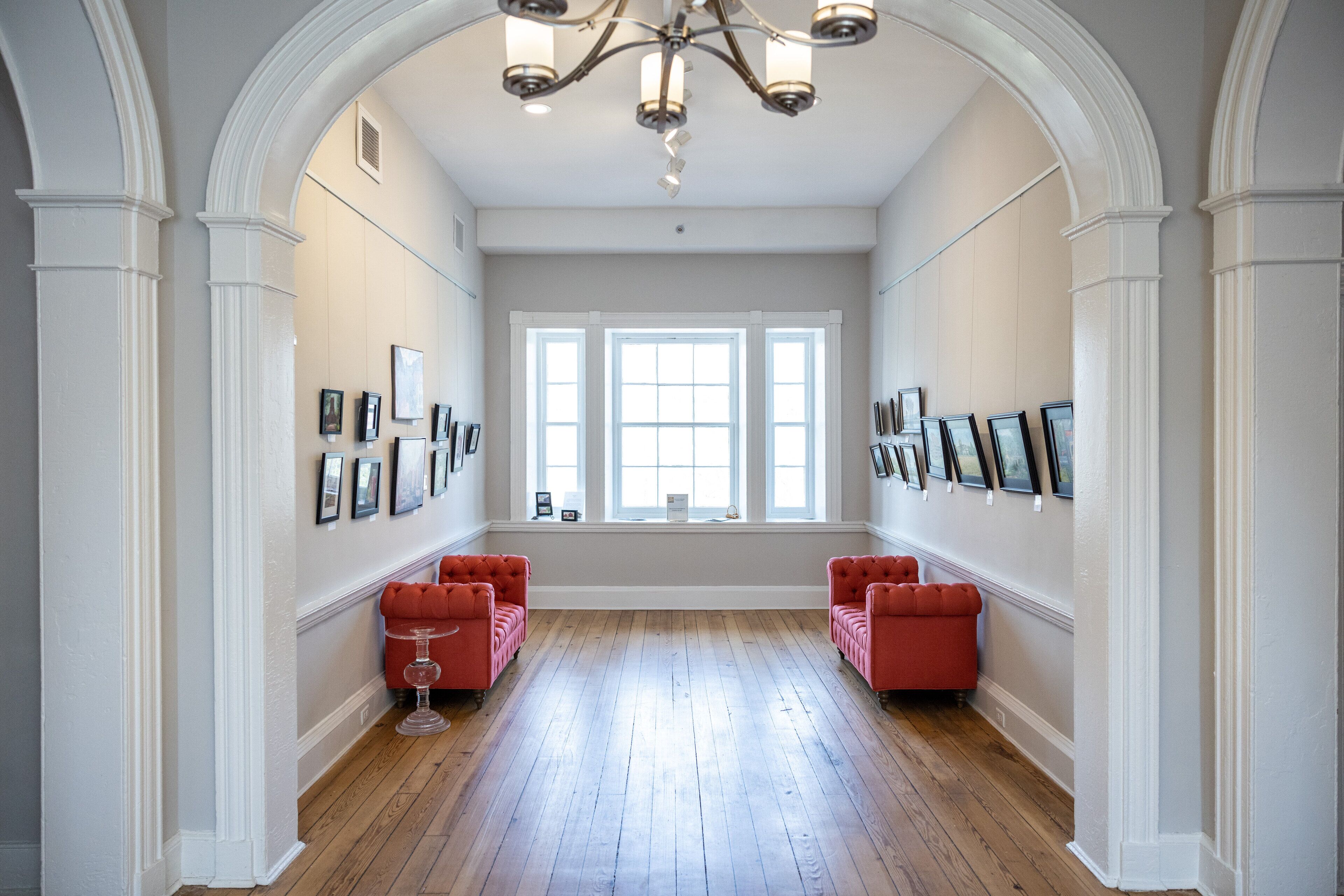 A spacious hallway with wooden flooring, white walls, and a large window at the end.