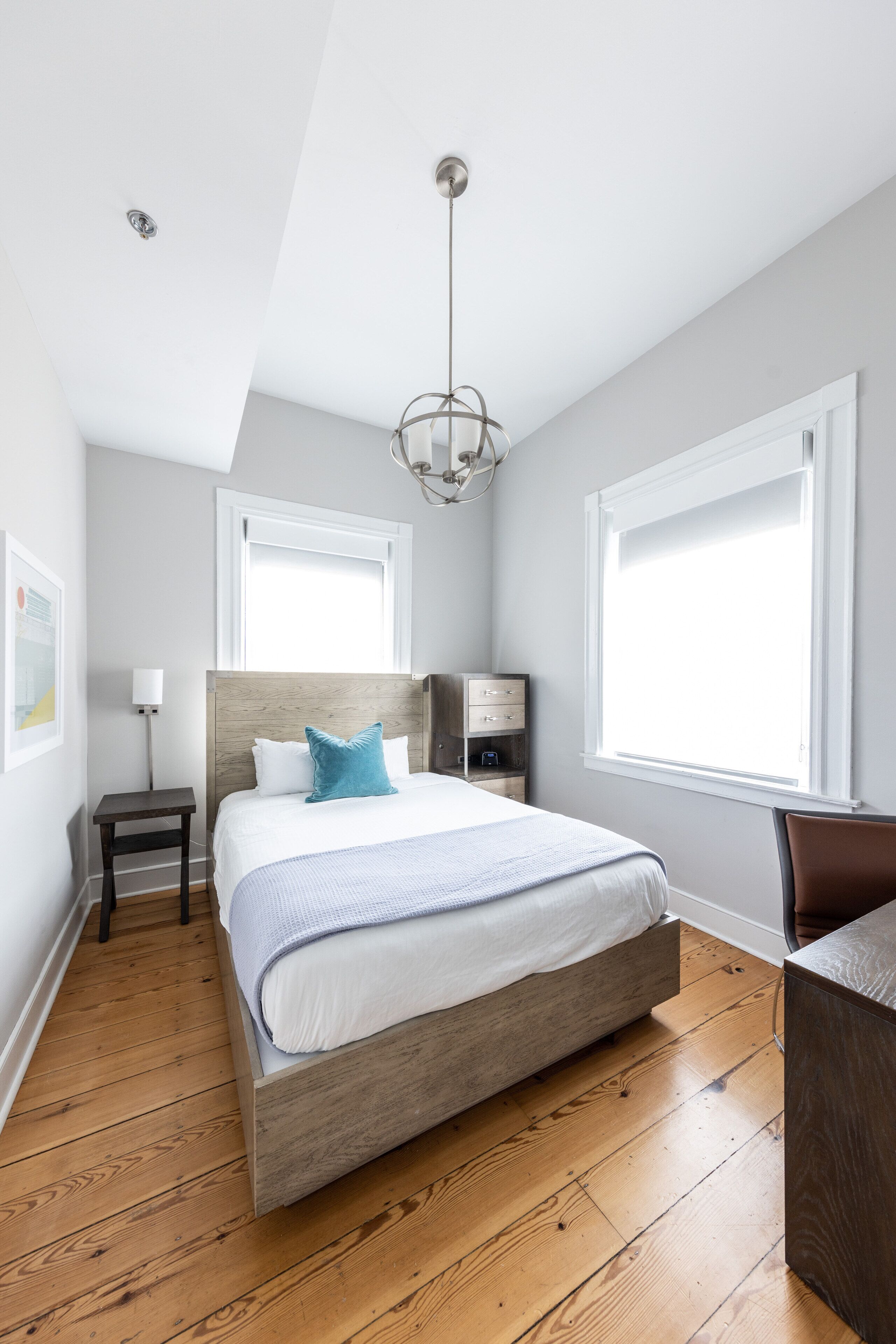 Un dormitorio moderno con una cama de madera, una mesita de noche, un escritorio y un ventanal grande.