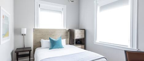 Un dormitorio moderno con una cama de madera, una mesita de noche, un escritorio y un ventanal grande.