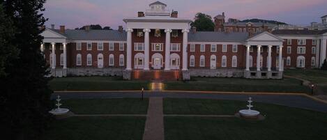 A large, symmetrical building with a central entrance flanked by columns, surrounded by a well-maintained lawn and a paved driveway.