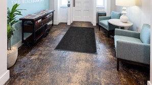 A hotel lobby with a reception desk, a coffee station, seating area, and an exit sign. - The Blackburn Inn and Conference Center (Staunton)