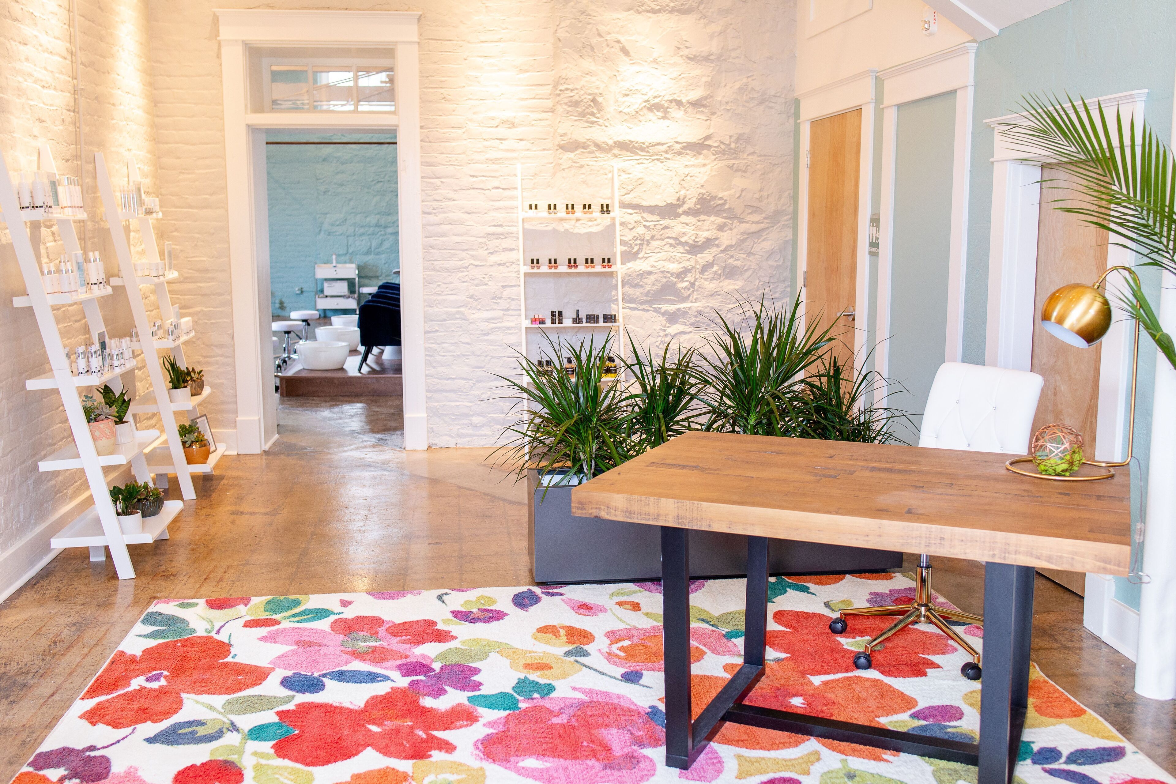 Een modern interieur met een houten bureau, een kleurrijk vloerkleed en planken met diverse spullen.