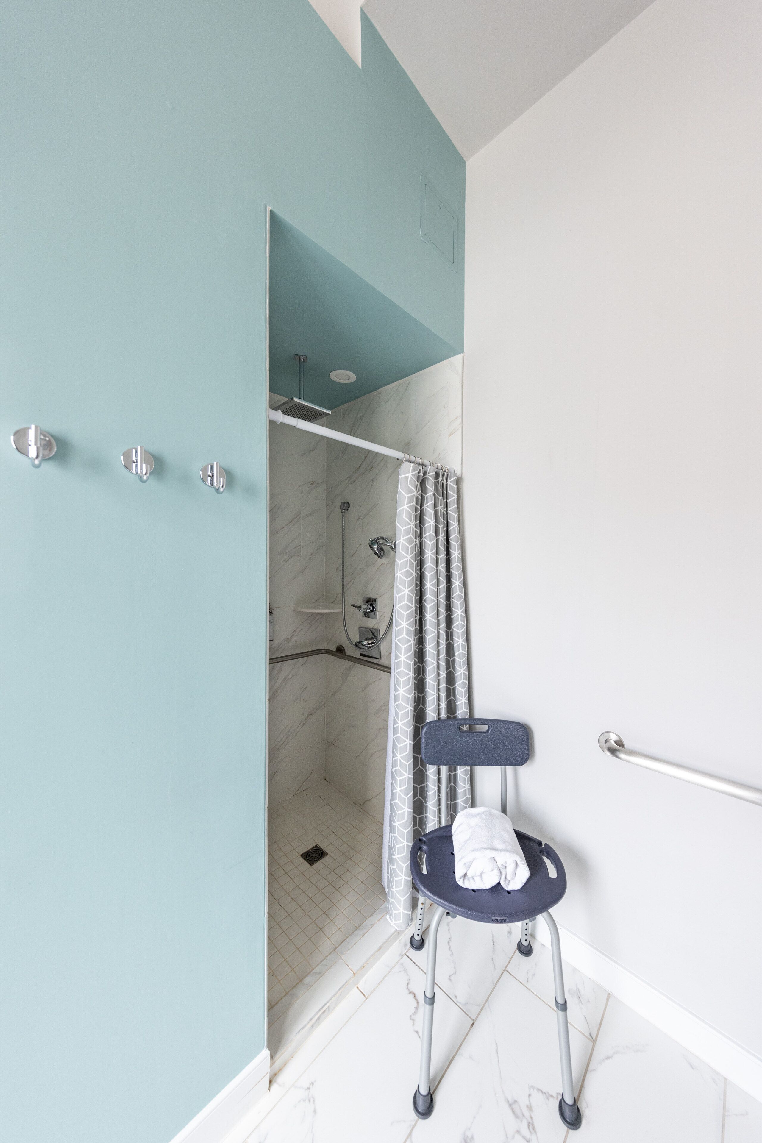 Une salle de bain équipée d’une douche, d’un porte-serviettes et d’un banc accessible aux personnes en fauteuil roulant.