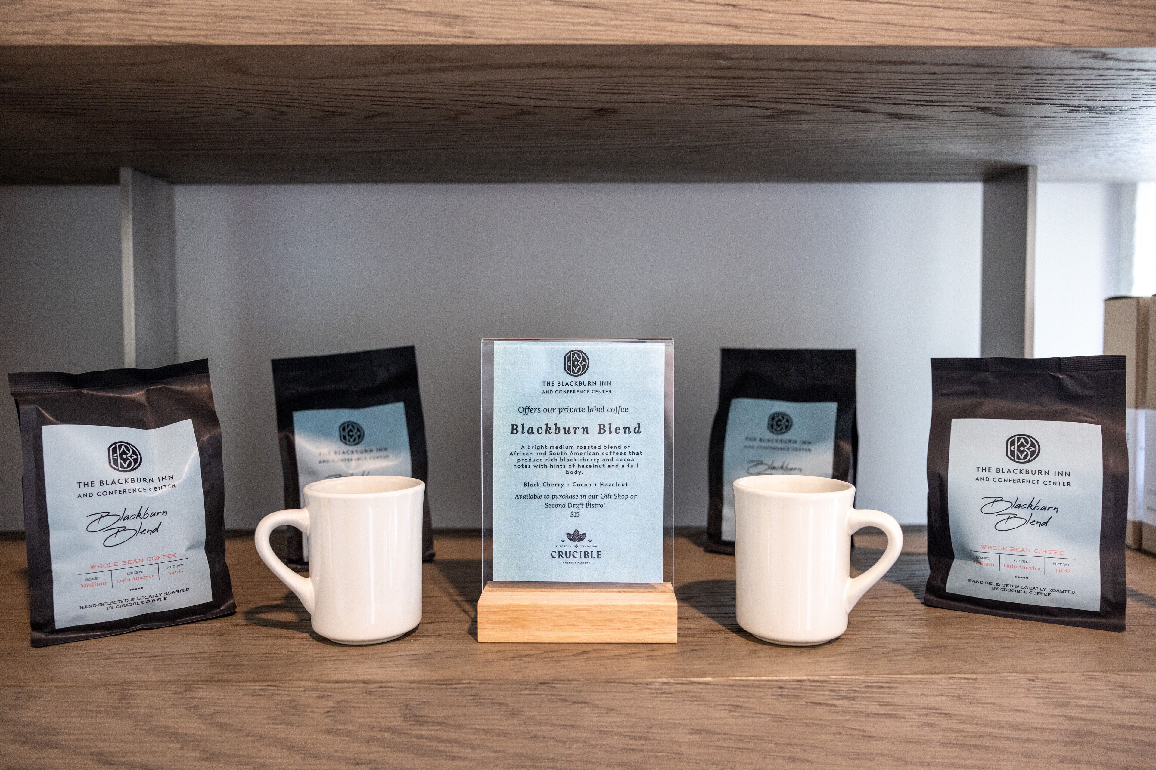 A display of coffee bags and mugs on a wooden shelf.