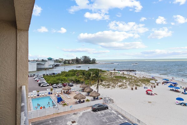 A beach view with a pool, umbrellas, and lounge chairs.
