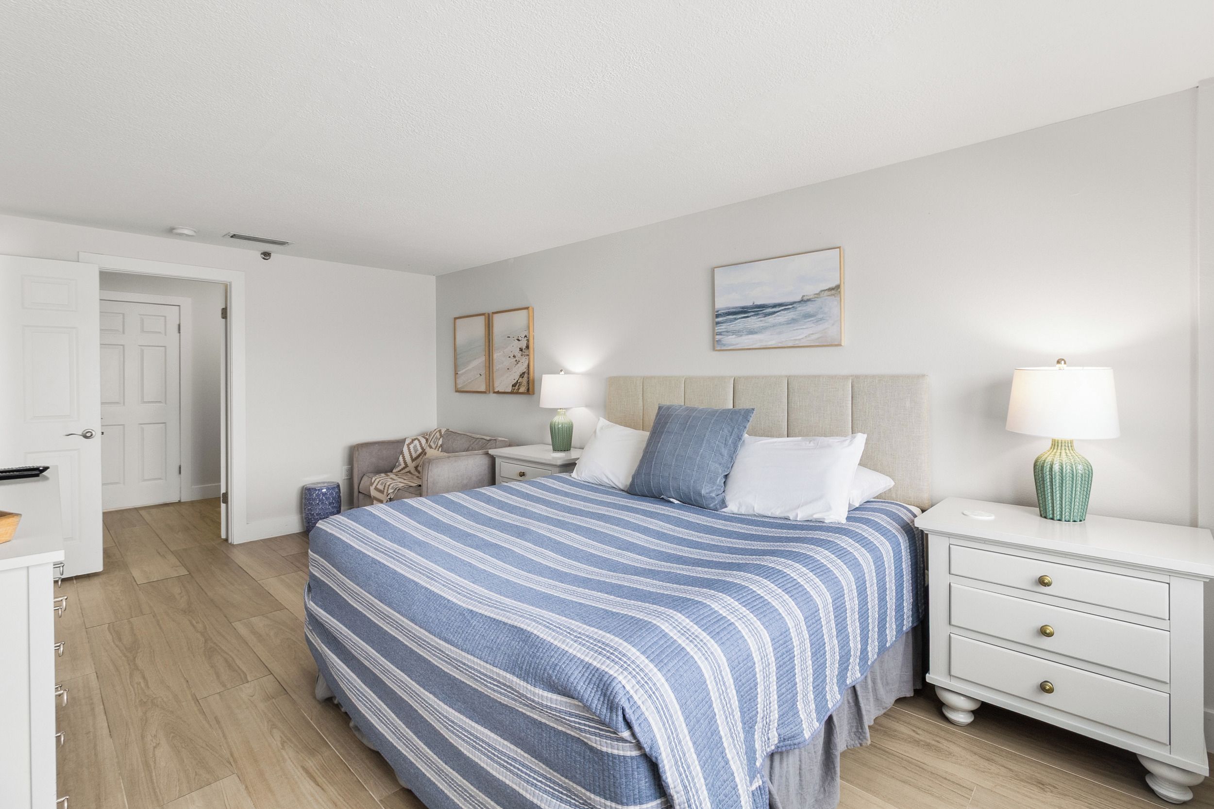 Ein Schlafzimmer mit einem Bett, Nachttischen, einem Beistelltisch, einem Sessel und einer Tür.