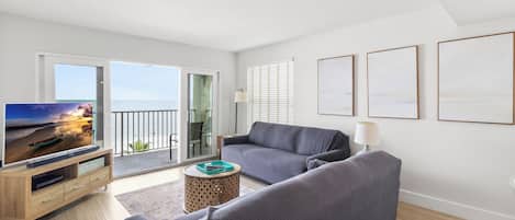 Un salón moderno con un sofá gris, un televisor sobre un mueble de madera y un balcón con vistas al mar.