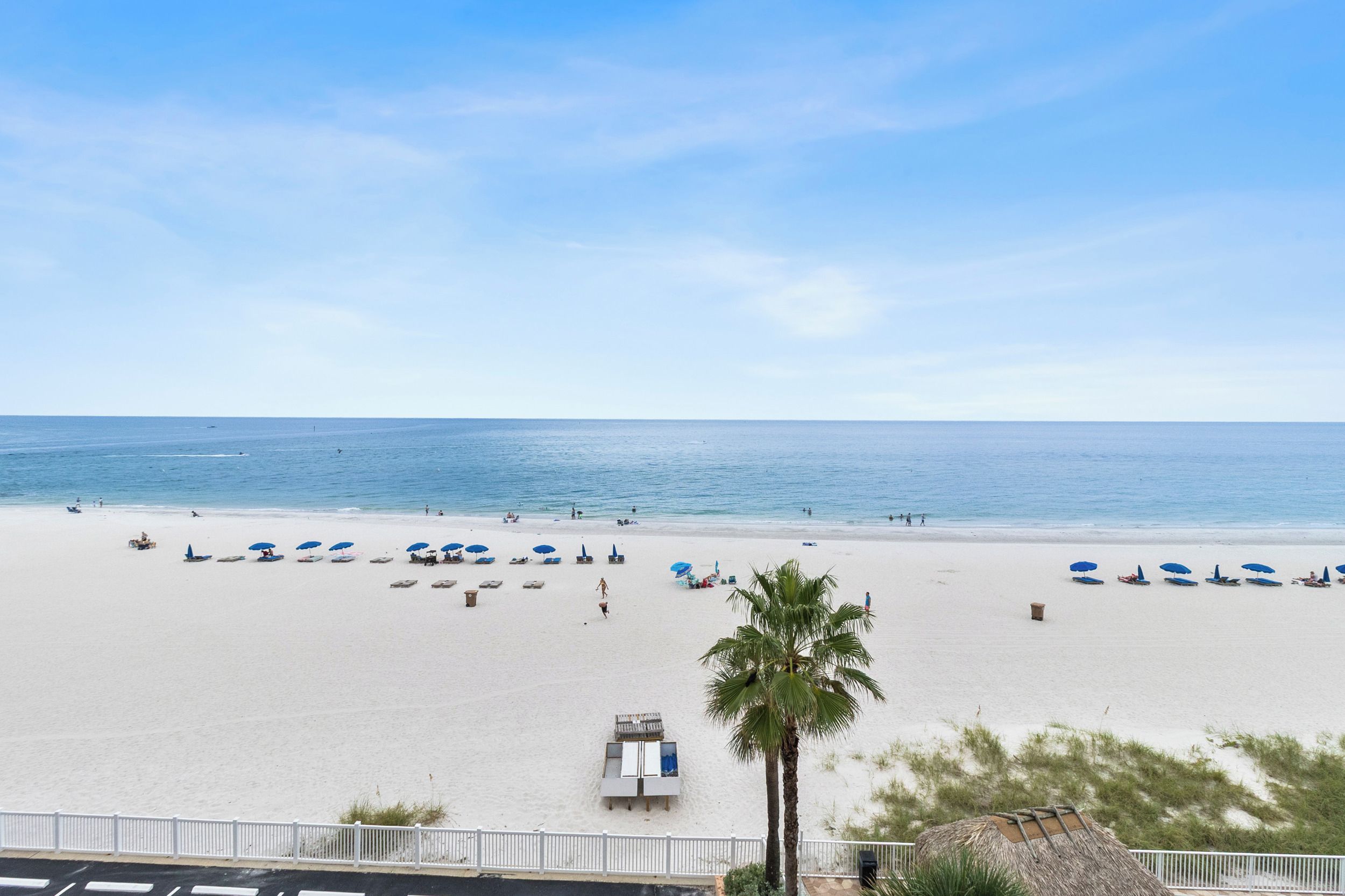 Una playa con arena blanca, sombrillas azules y una palmera.
