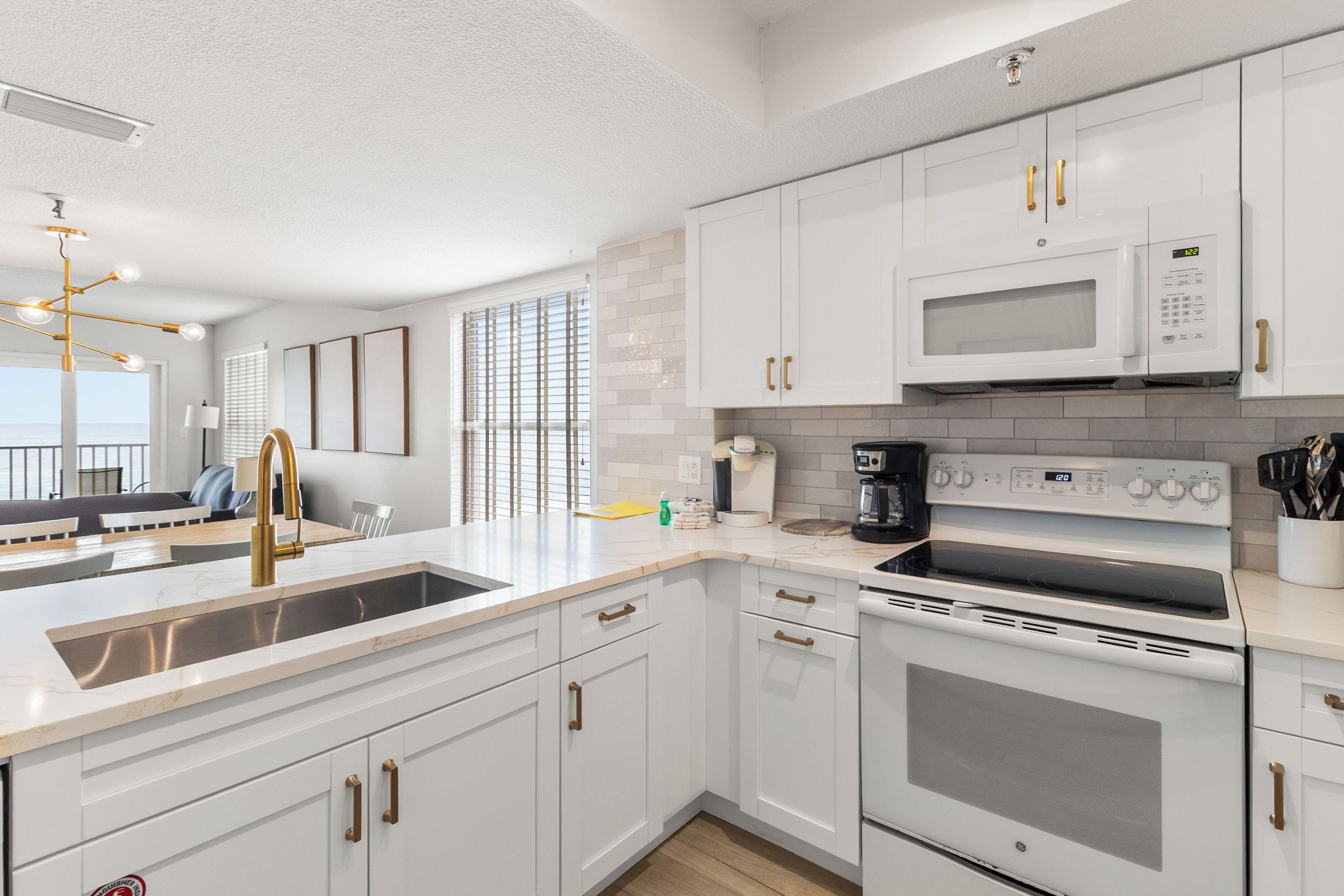 A modern kitchen with white cabinets, a stainless steel sink, a built-in microwave, and a stove.